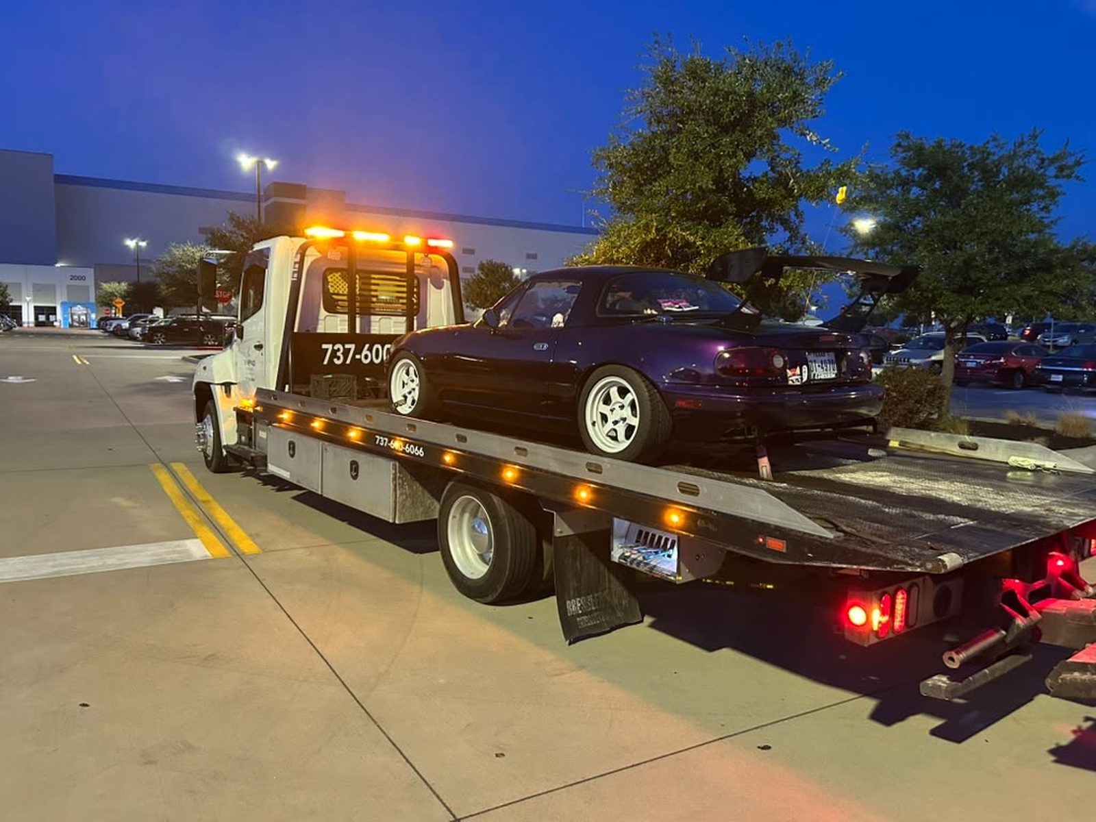 Sinbad Towing flatbed truck with beacon lights on, loading a car at night